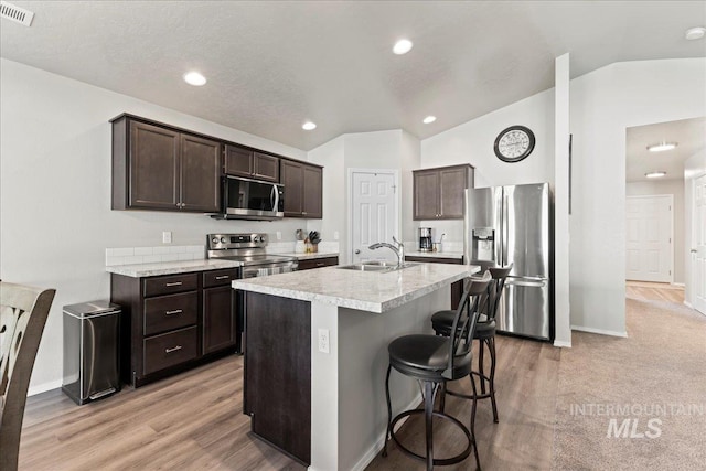 kitchen featuring appliances with stainless steel finishes, a sink, dark brown cabinets, light countertops, and vaulted ceiling