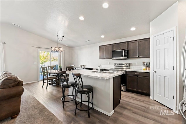 kitchen with appliances with stainless steel finishes, a sink, dark brown cabinetry, lofted ceiling, and light countertops