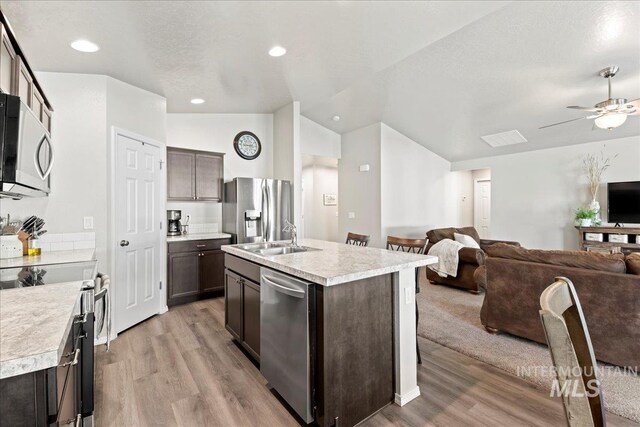 kitchen featuring stainless steel appliances, a sink, open floor plan, light wood-style floors, and lofted ceiling