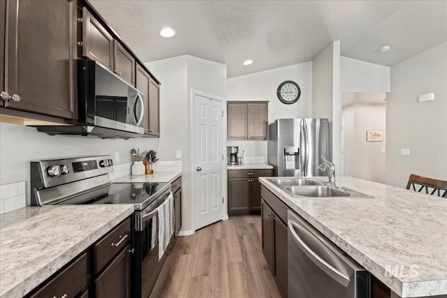 kitchen featuring stainless steel appliances, a sink, light wood-style floors, an island with sink, and light countertops