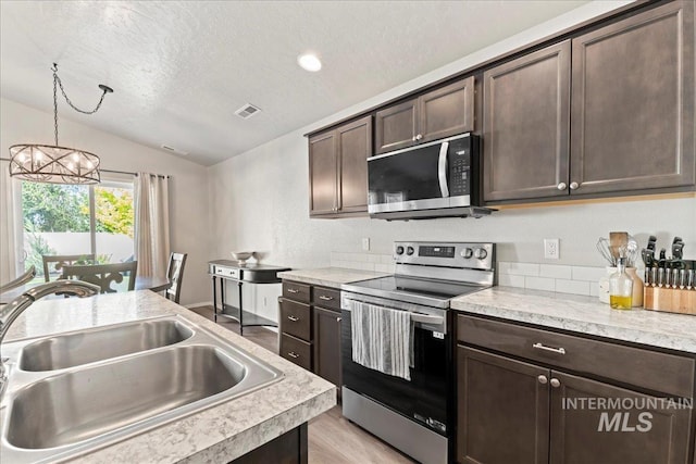 kitchen featuring appliances with stainless steel finishes, a sink, vaulted ceiling, dark brown cabinets, and a textured ceiling