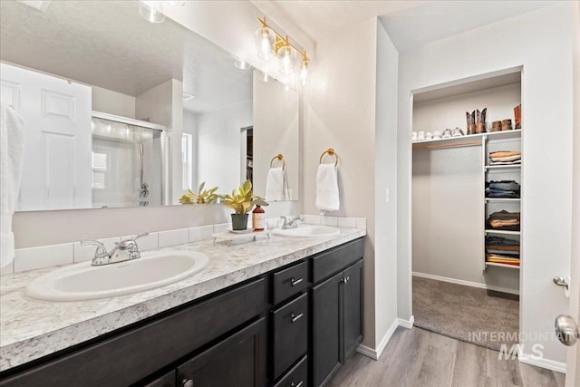 full bath featuring a shower stall, a spacious closet, double vanity, wood finished floors, and baseboards