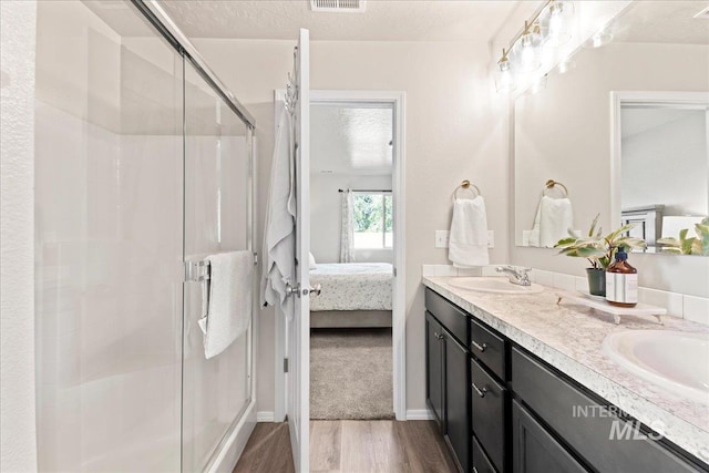 ensuite bathroom featuring wood finished floors, a shower stall, double vanity, and baseboards