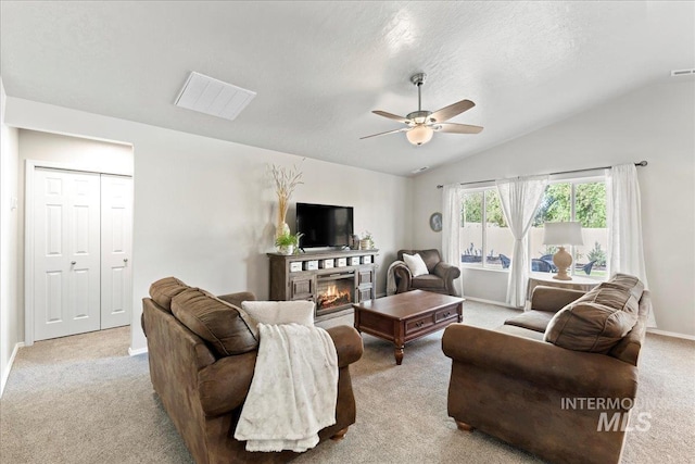carpeted living room featuring a glass covered fireplace, lofted ceiling, a ceiling fan, baseboards, and a textured ceiling