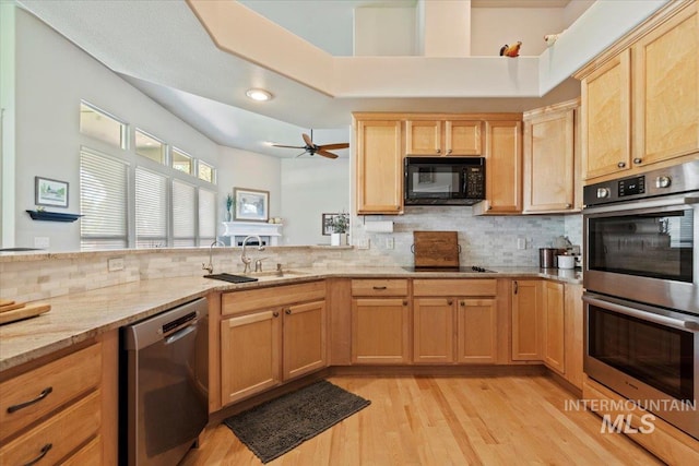 kitchen with black appliances, decorative backsplash, a sink, light wood-style flooring, and light stone countertops