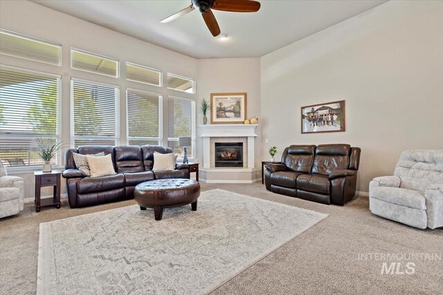 carpeted living area featuring ceiling fan, baseboards, and a glass covered fireplace
