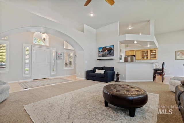 living room featuring arched walkways, light colored carpet, high vaulted ceiling, plenty of natural light, and a ceiling fan