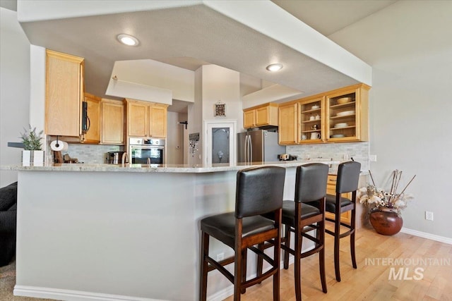 kitchen featuring appliances with stainless steel finishes, a peninsula, tasteful backsplash, glass insert cabinets, and recessed lighting