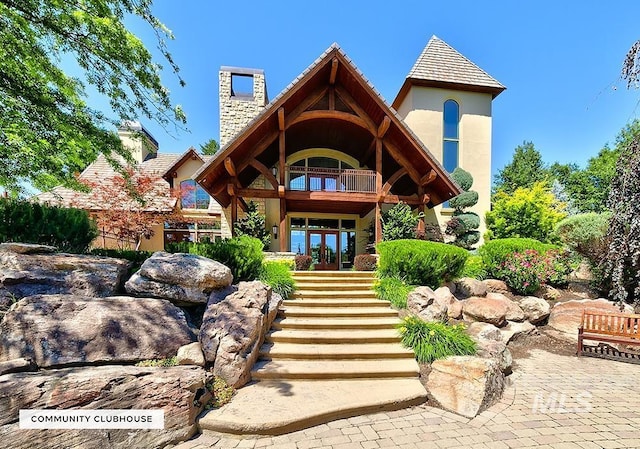 back of house featuring a balcony, a chimney, stairway, french doors, and stucco siding