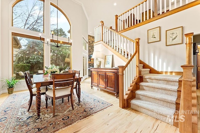 dining area with ornamental molding, light wood-type flooring, a towering ceiling, and stairs