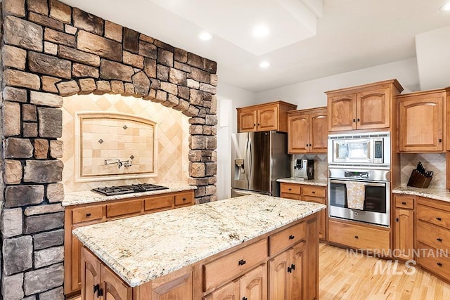 kitchen featuring light wood finished floors, stainless steel appliances, light stone counters, and decorative backsplash