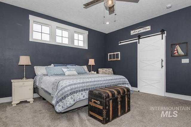 bedroom with ceiling fan, a barn door, carpet flooring, and a textured ceiling