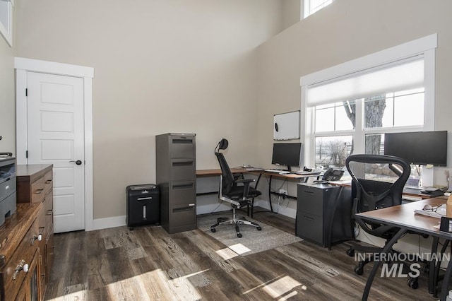 office space with a wealth of natural light, a towering ceiling, and dark hardwood / wood-style flooring