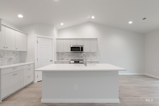 kitchen with a center island with sink, light wood-style flooring, light countertops, vaulted ceiling, and appliances with stainless steel finishes