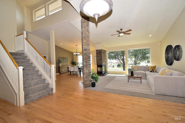 living area featuring a healthy amount of sunlight, wood finished floors, ceiling fan with notable chandelier, and stairs