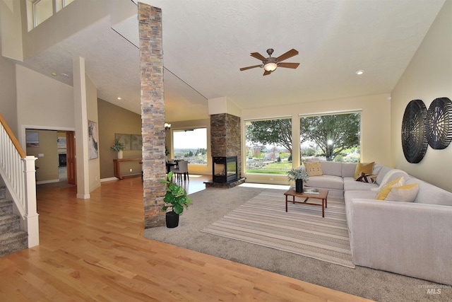 living room with decorative columns, a ceiling fan, a stone fireplace, wood finished floors, and stairs