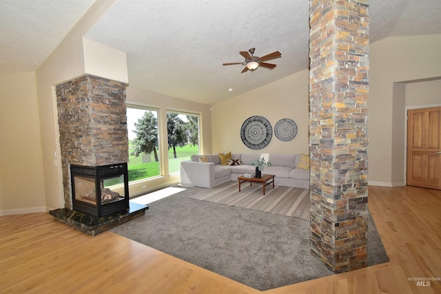 living room featuring vaulted ceiling, a textured ceiling, a ceiling fan, decorative columns, and wood finished floors