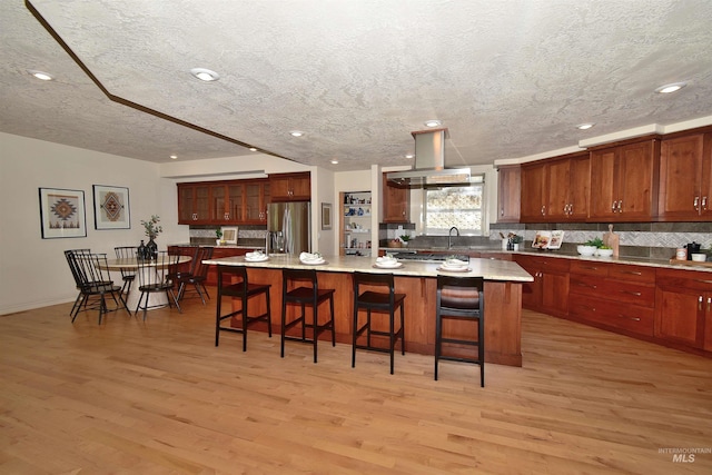 kitchen featuring island range hood, stainless steel fridge, light wood-style floors, and a textured ceiling