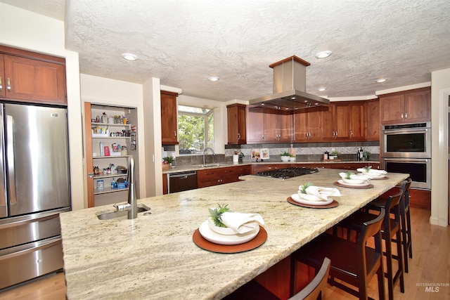 kitchen featuring light stone countertops, appliances with stainless steel finishes, island range hood, a breakfast bar area, and backsplash