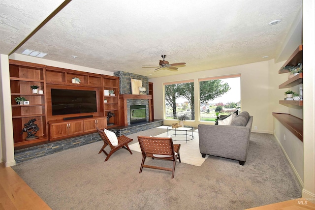 carpeted living area featuring visible vents, baseboards, a stone fireplace, ceiling fan, and a textured ceiling