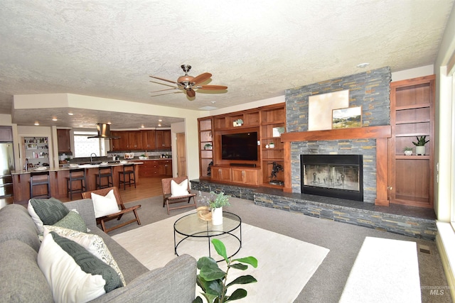 carpeted living area featuring a textured ceiling, ceiling fan, a sink, and a stone fireplace