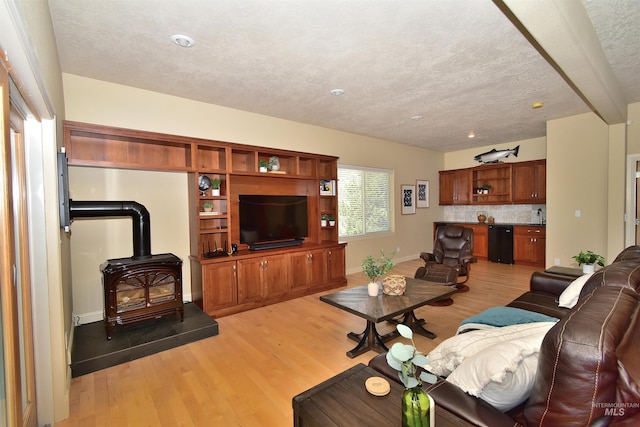 living room with a wood stove, light wood finished floors, a textured ceiling, and baseboards