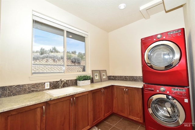 clothes washing area featuring a sink, dark tile patterned floors, cabinet space, and stacked washer / drying machine