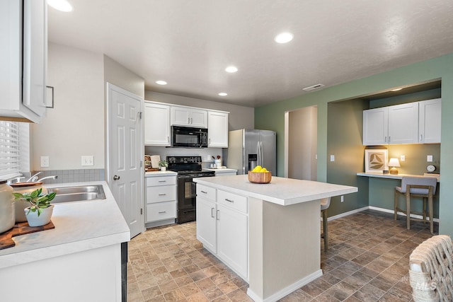 kitchen with a breakfast bar, black appliances, white cabinets, sink, and a kitchen island