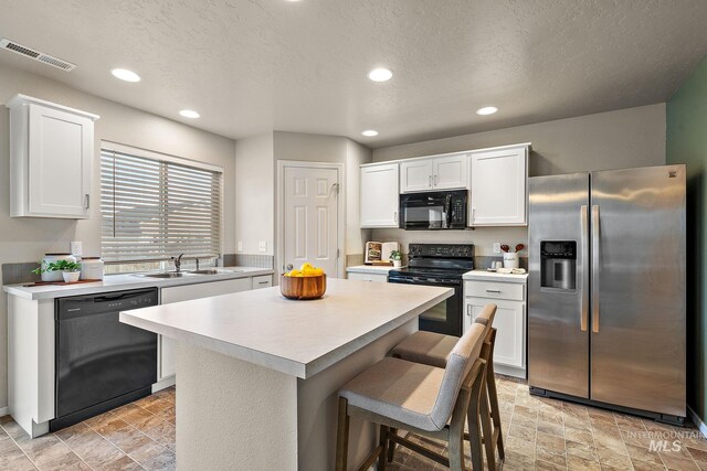 kitchen featuring a center island, black appliances, sink, white cabinetry, and a breakfast bar area