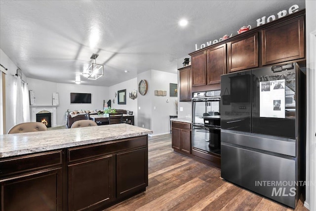 1430 NE Quigley St, Mountain Home, ID 83647 - kitchen featuring dark wood-style flooring, open floor plan, dark brown cabinetry, black appliances, and a lit fireplace