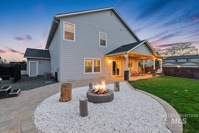 1430 NE Quigley St, Mountain Home, ID 83647 - back of house at dusk featuring a yard, an outdoor fire pit, a patio, fence, and central AC unit