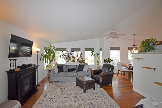 living area with a glass covered fireplace, baseboards, lofted ceiling, and dark wood finished floors