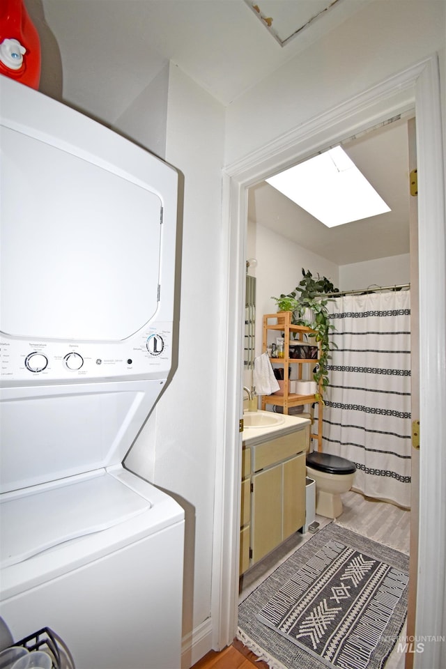 clothes washing area with stacked washing maching and dryer, laundry area, a skylight, light wood-style flooring, and a sink