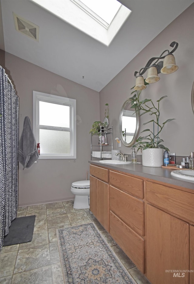 bathroom with vaulted ceiling with skylight, toilet, visible vents, and a sink