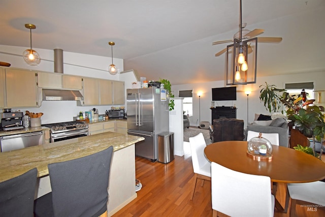 kitchen with wood finished floors, stainless steel appliances, under cabinet range hood, decorative light fixtures, and open floor plan