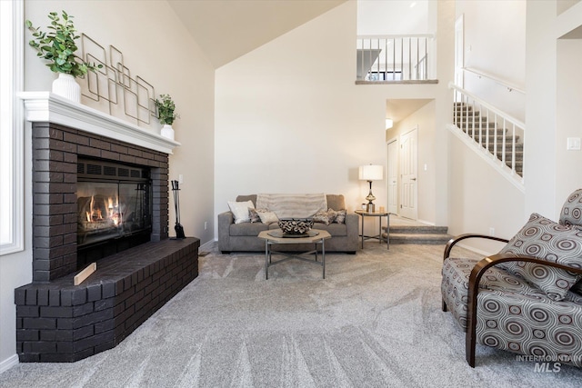 carpeted living room with stairway, a brick fireplace, baseboards, and high vaulted ceiling