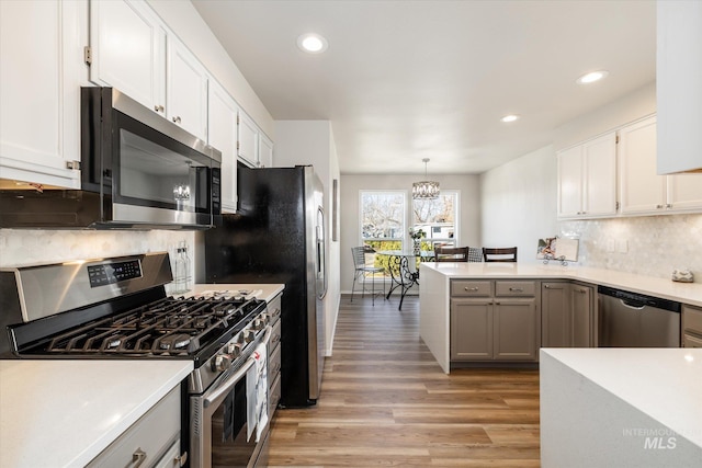 kitchen featuring light wood-style flooring, tasteful backsplash, a peninsula, appliances with stainless steel finishes, and light countertops