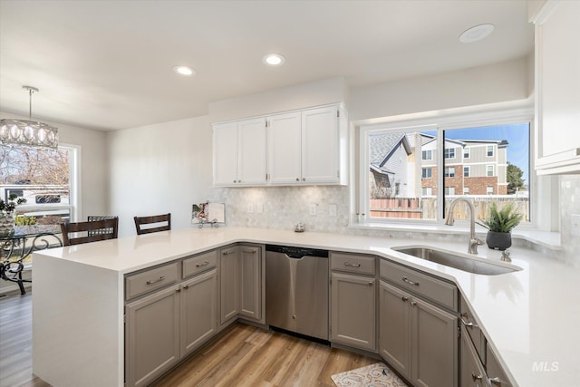 kitchen with gray cabinetry, a sink, a peninsula, light countertops, and dishwasher