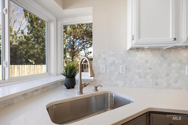 kitchen with a sink, decorative backsplash, white cabinetry, and light countertops