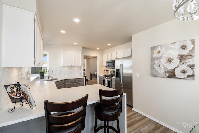 kitchen with light countertops, decorative backsplash, appliances with stainless steel finishes, a peninsula, and a sink