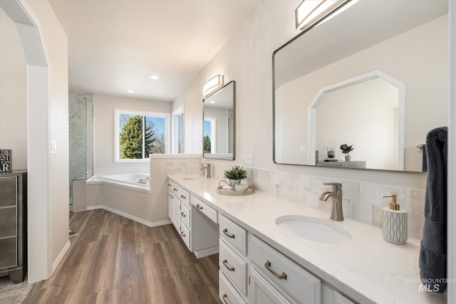 full bathroom with a garden tub, wood finished floors, double vanity, and a sink