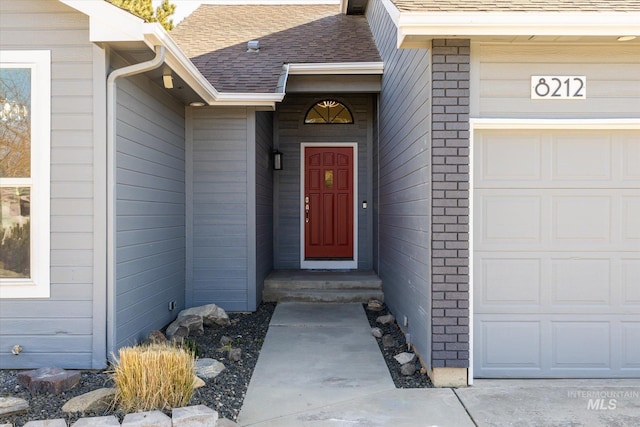 view of exterior entry with brick siding, an attached garage, and a shingled roof