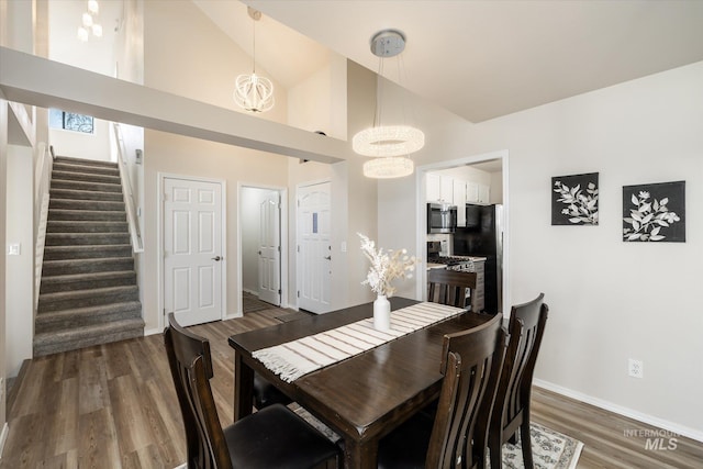 dining area with wood finished floors, baseboards, high vaulted ceiling, stairs, and a chandelier