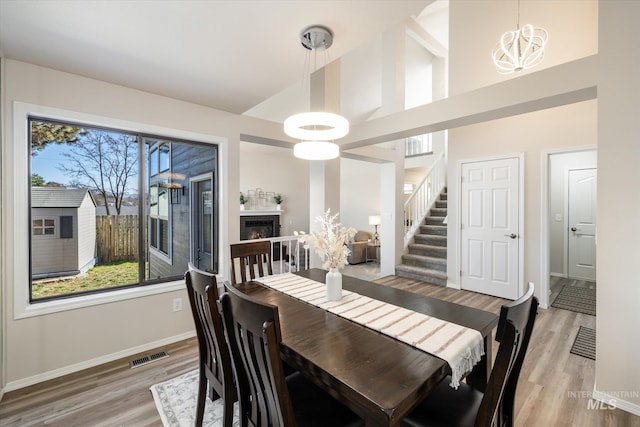 dining space featuring visible vents, a notable chandelier, a glass covered fireplace, stairway, and light wood finished floors