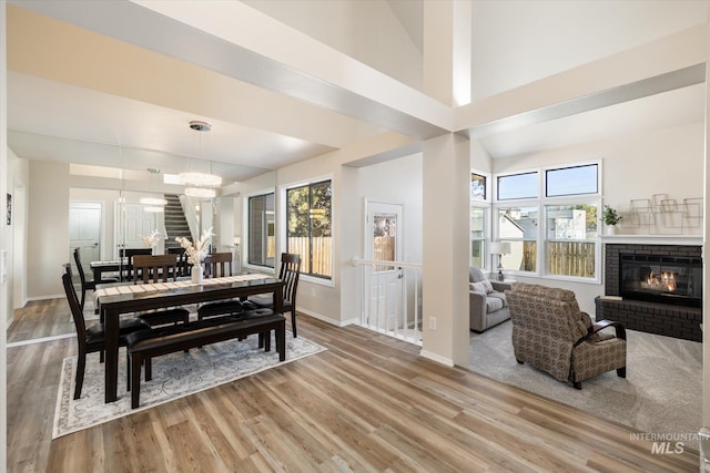 dining area with a brick fireplace, baseboards, a chandelier, a high ceiling, and light wood-style floors