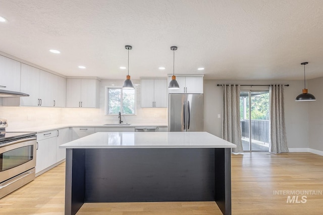 kitchen with sink, hanging light fixtures, light hardwood / wood-style flooring, appliances with stainless steel finishes, and white cabinetry