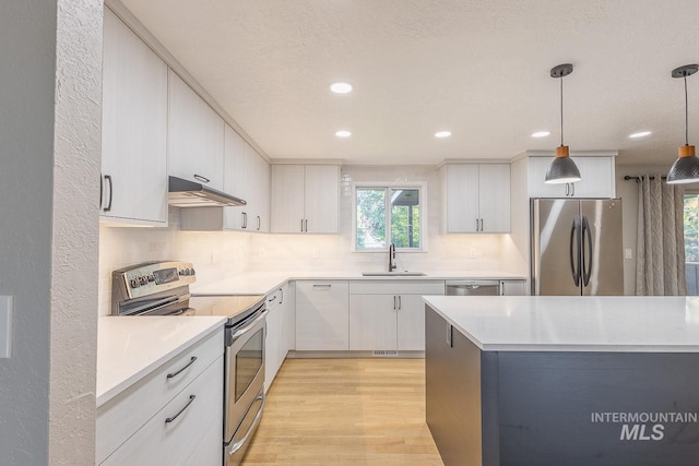 kitchen with appliances with stainless steel finishes, sink, light hardwood / wood-style floors, white cabinetry, and hanging light fixtures