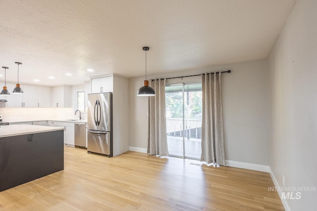 kitchen featuring white cabinets, appliances with stainless steel finishes, light wood-type flooring, and pendant lighting