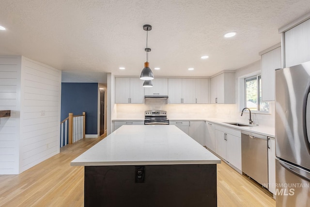 kitchen featuring appliances with stainless steel finishes, a center island, decorative light fixtures, and light hardwood / wood-style floors