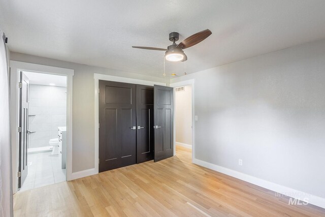 unfurnished bedroom featuring connected bathroom, light hardwood / wood-style flooring, a closet, and ceiling fan